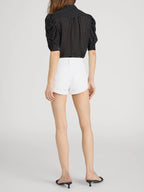 Person wearing a black polka dot blouse and white shorts on a light gray background