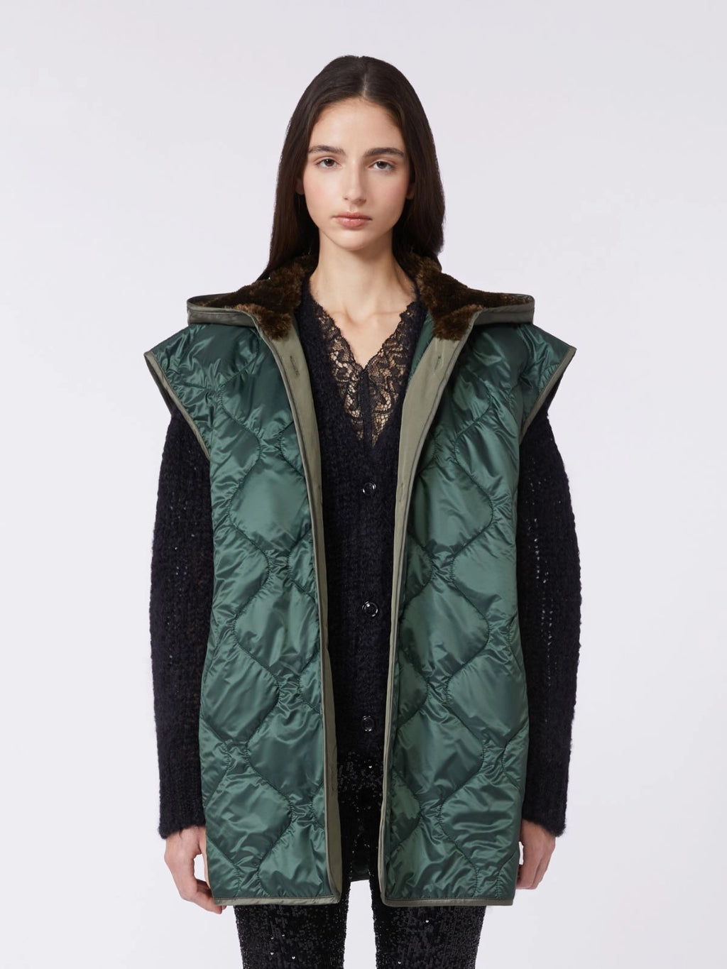 Woman wearing a green quilted vest over a black outfit on a white background
