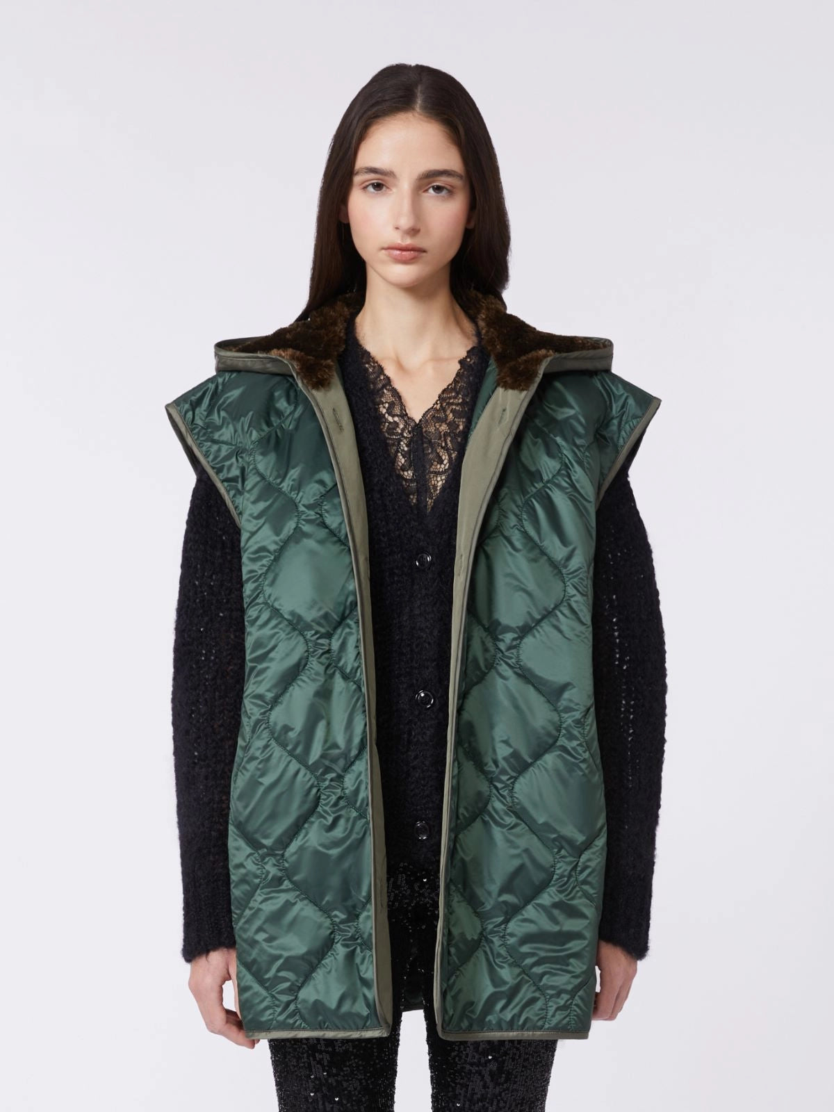 Woman wearing a green quilted vest over a black outfit on a white background