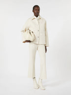 Person wearing a white outfit holding a matching handbag on a white background