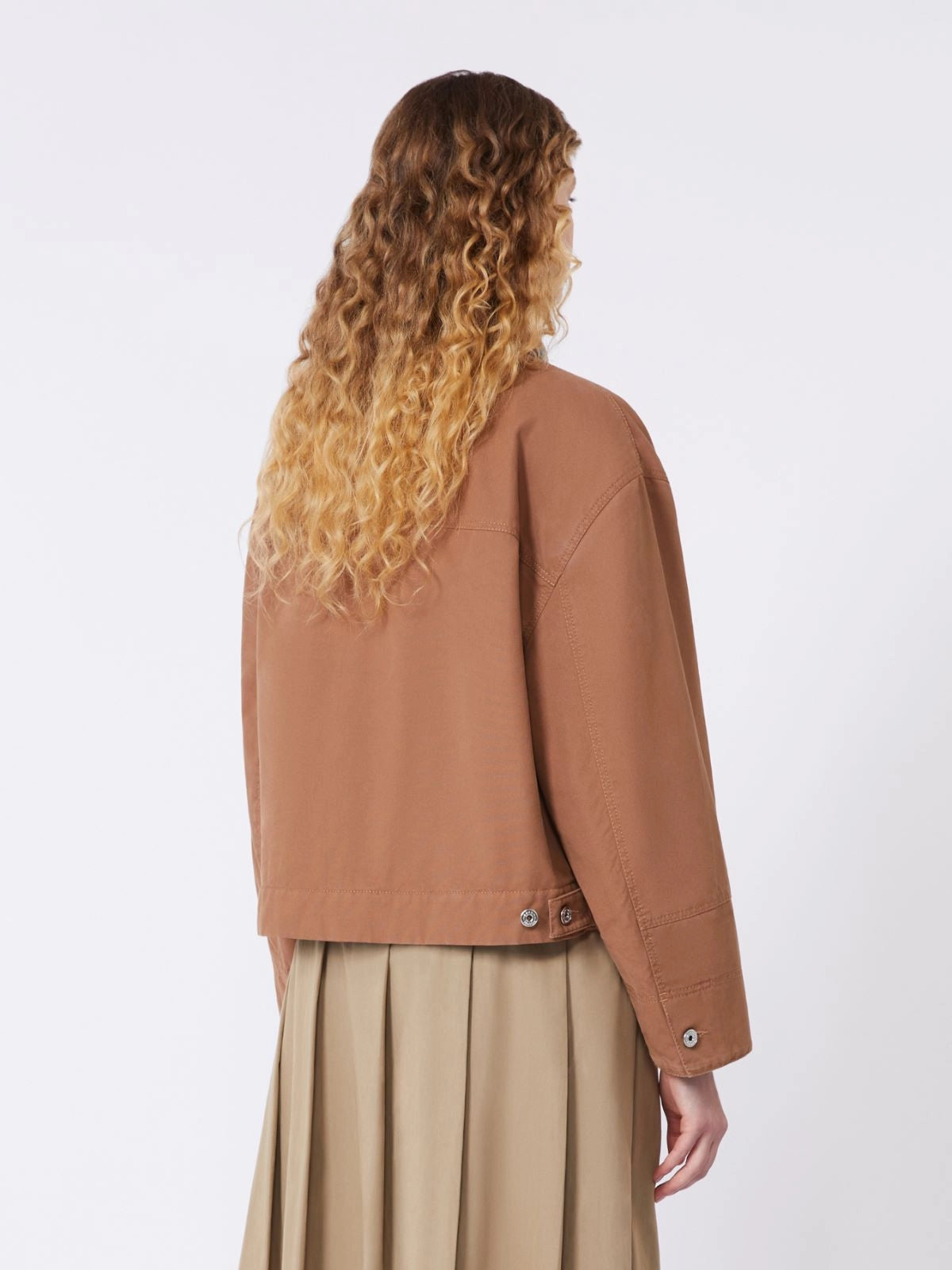 Person wearing a brown jacket and beige skirt on a white background