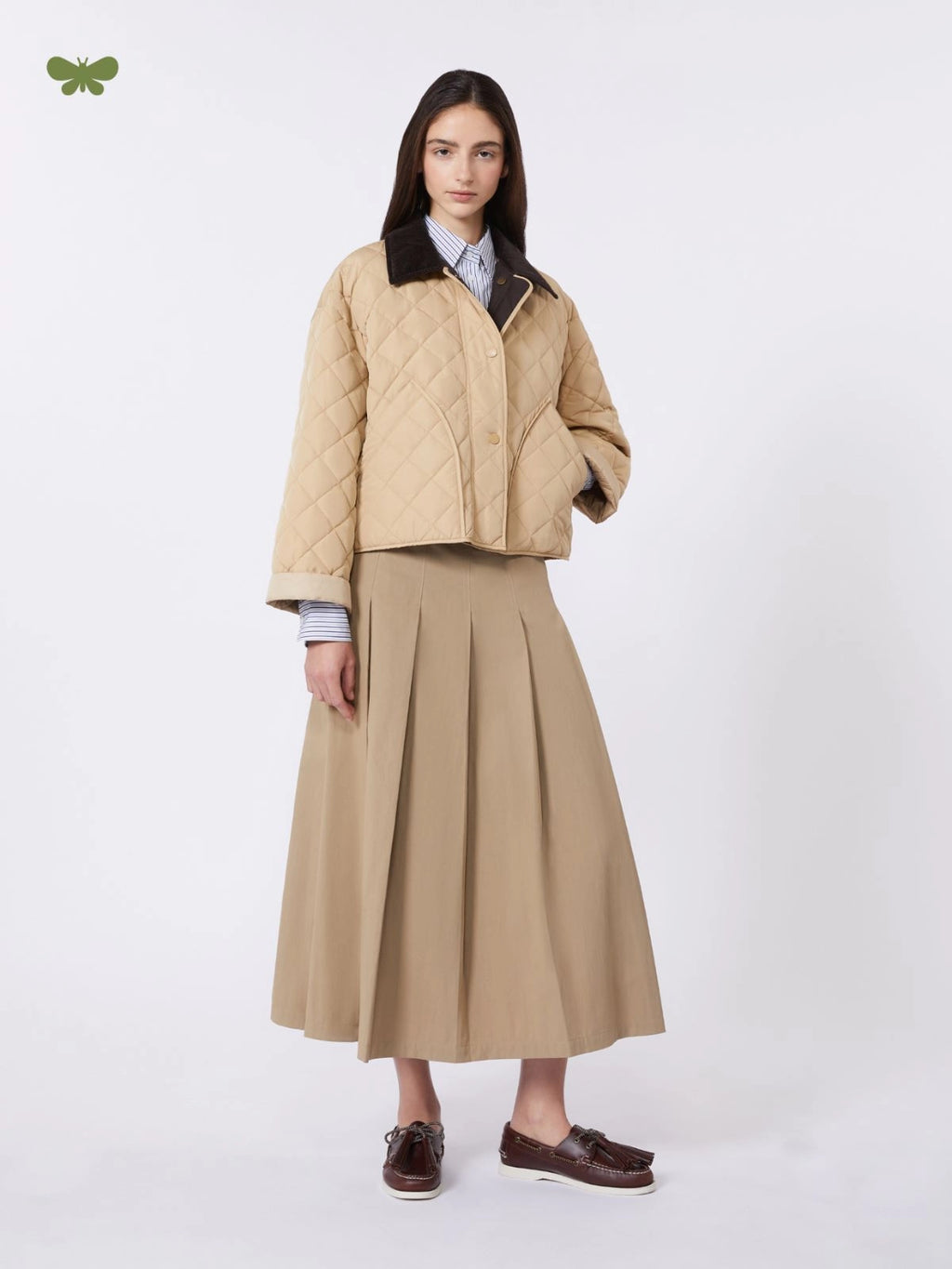 Woman wearing a beige quilted jacket and pleated skirt on a white background