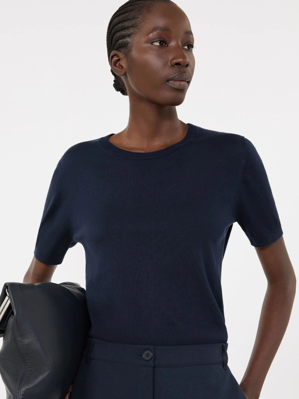 Woman wearing a navy blue top holding a black bag against a white background