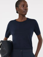 Woman wearing a navy blue top holding a black bag against a white background