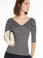 A woman wearing a striped V-neck sweater with three-quarter sleeves, paired with a white skirt and carrying a beige clutch.