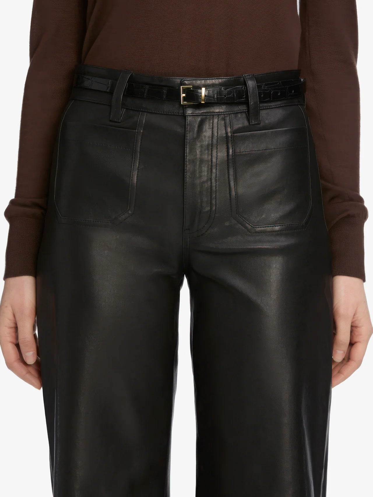 Person wearing black leather pants with a brown long-sleeve shirt on a white background