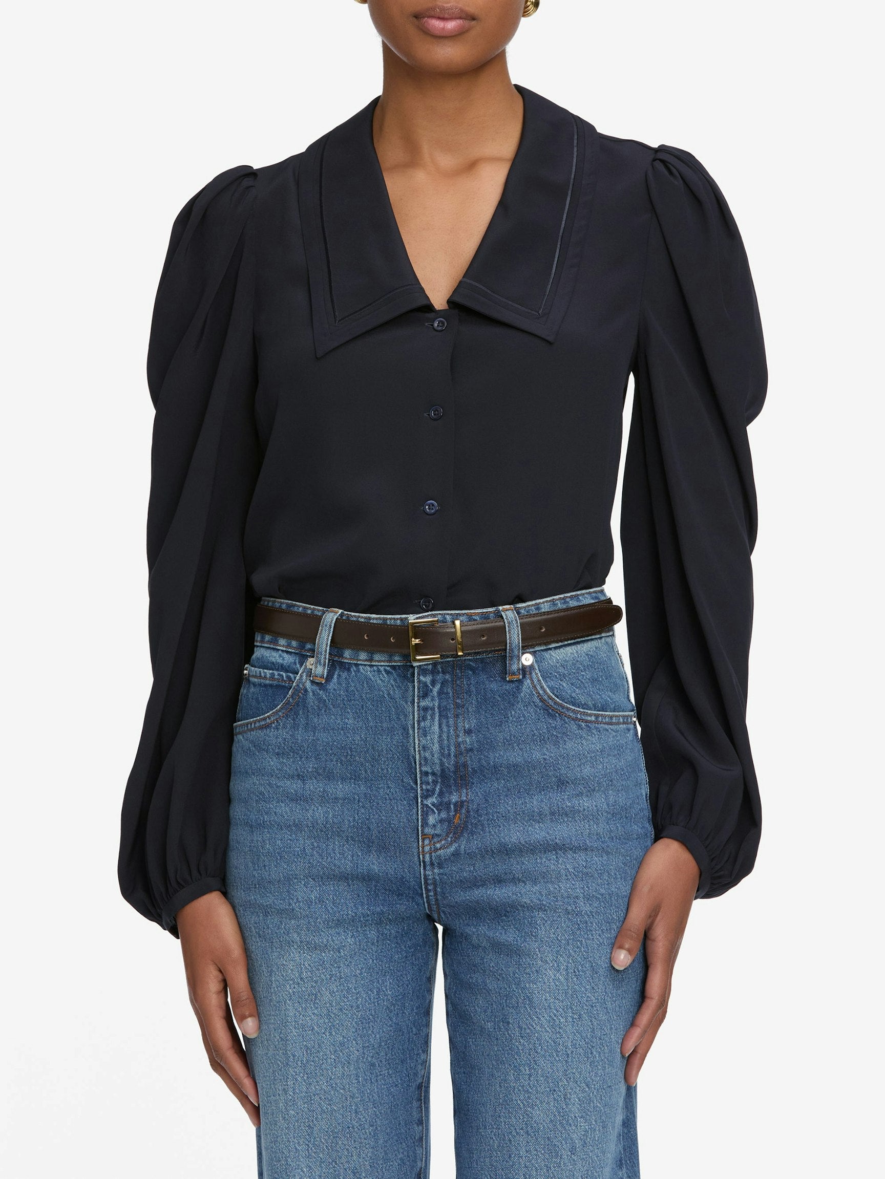 Person wearing a navy blouse with puffed sleeves and blue jeans on a white background