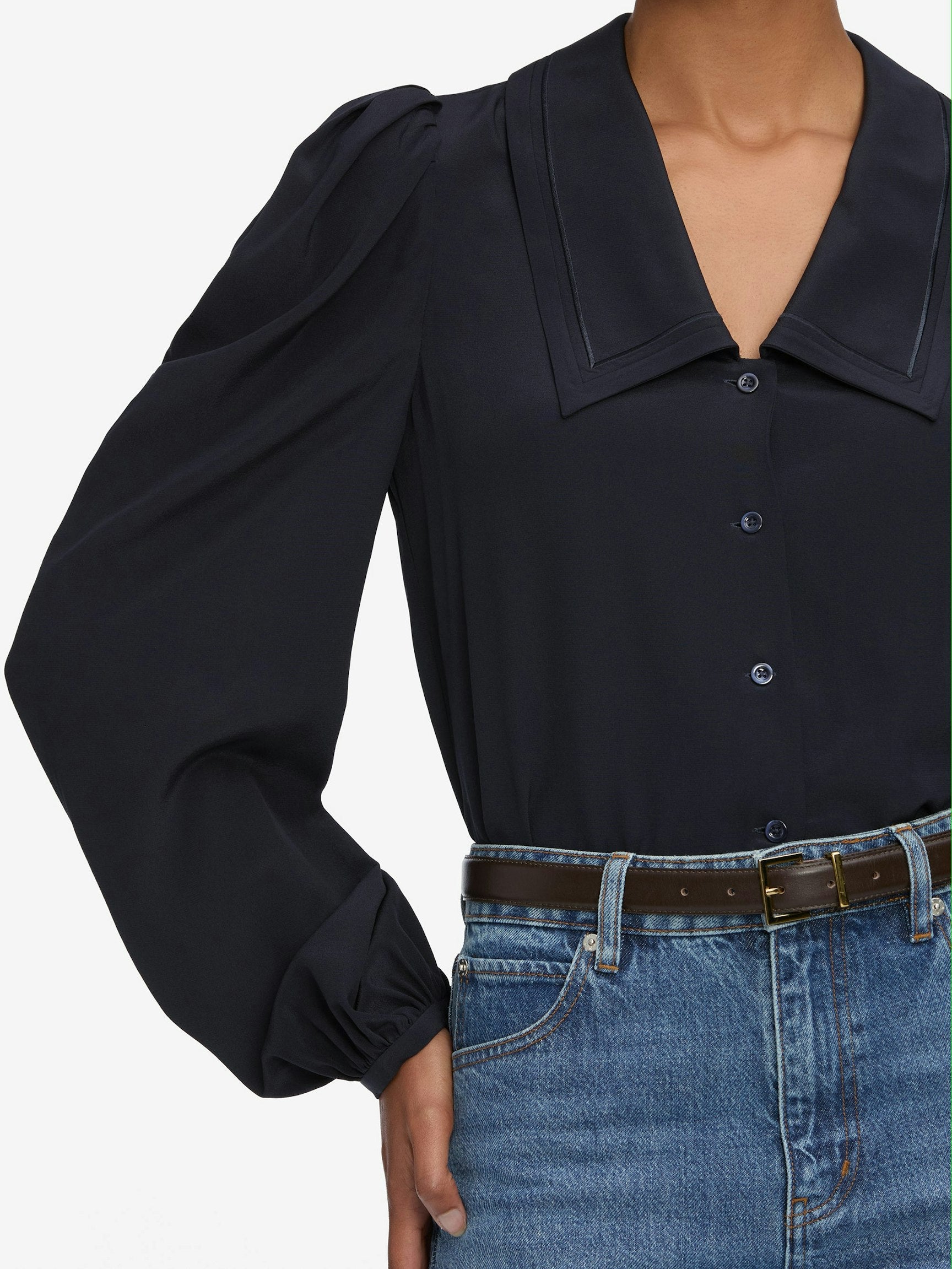 Navy blouse with puffed sleeves and blue jeans on a plain background