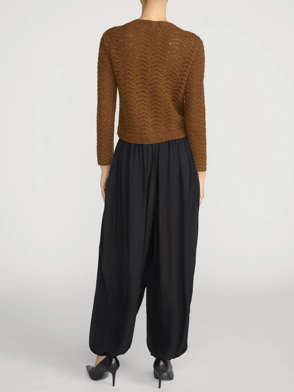 A model shown from the back wearing a textured brown cropped sweater and black wide-leg pants, paired with black high heels, against a light gray studio background.
