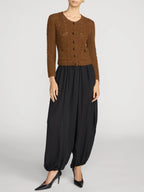 A model wearing a brown textured knit cardigan with dark buttons, paired with black balloon pants and black pointed-toe heels, photographed against a light gray studio background.