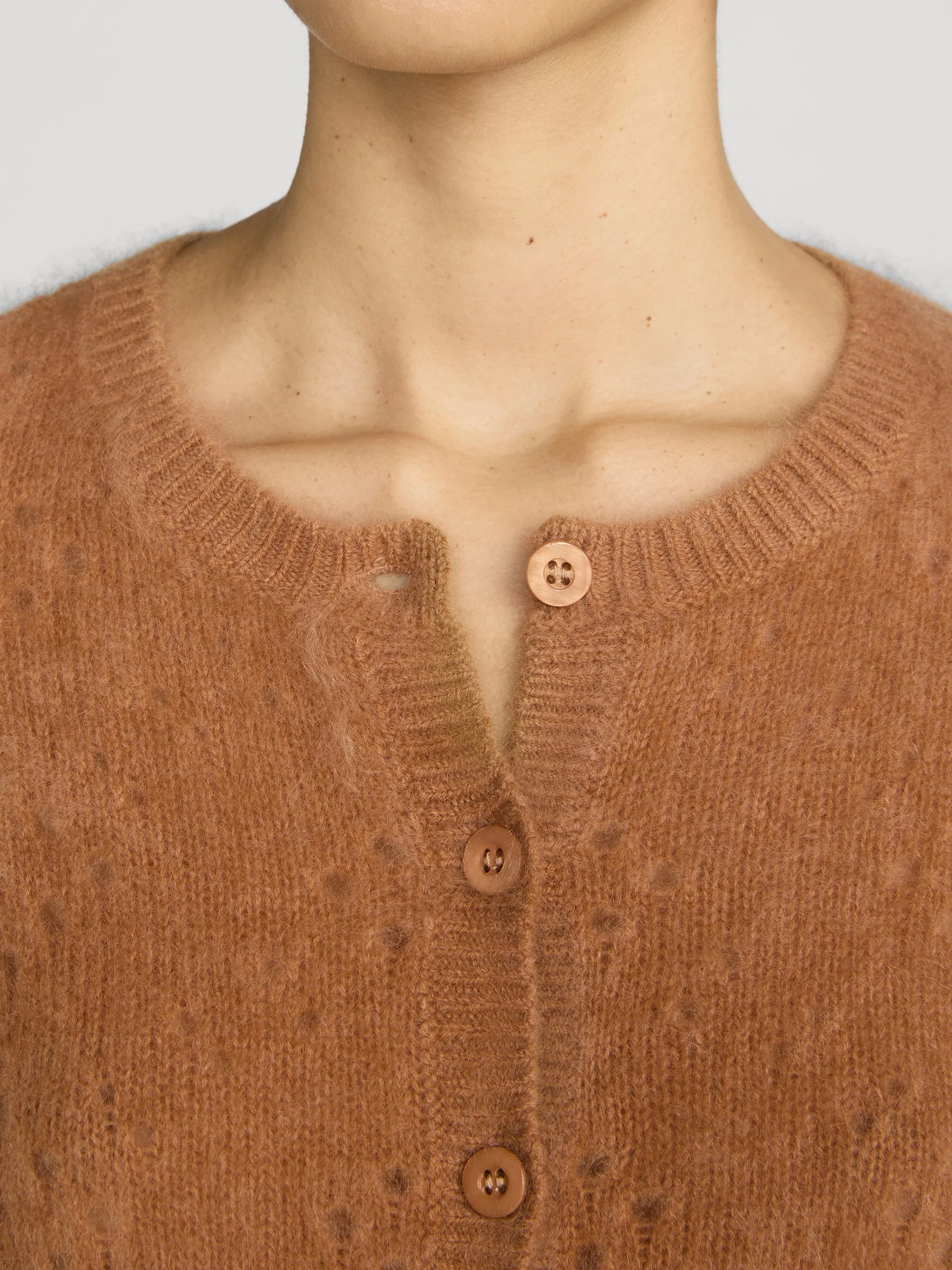 Close-up of a person wearing a warm rust-brown knit cardigan sweater with a buttoned henley neckline.