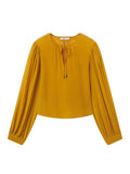 A mustard yellow long-sleeve blouse with a round neckline, front tie detail, and gathered sleeves, shown flat on a light gray background.
