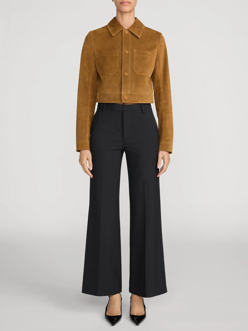 A model is shown from the neck down wearing a cropped tan suede jacket and black wide-leg trousers against a light gray studio background.