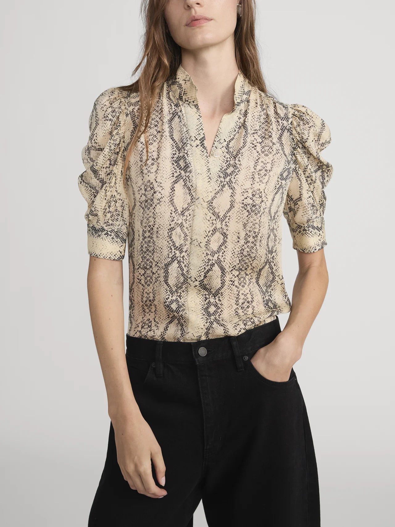 Woman wearing a snake print blouse with black pants on a plain background