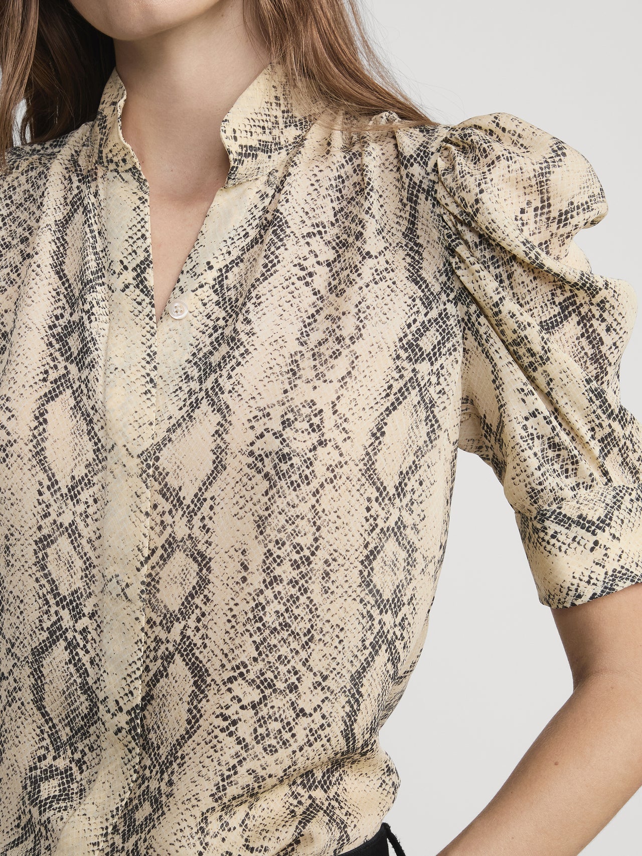 Close-up of a person wearing a patterned blouse with puff sleeves on a plain background