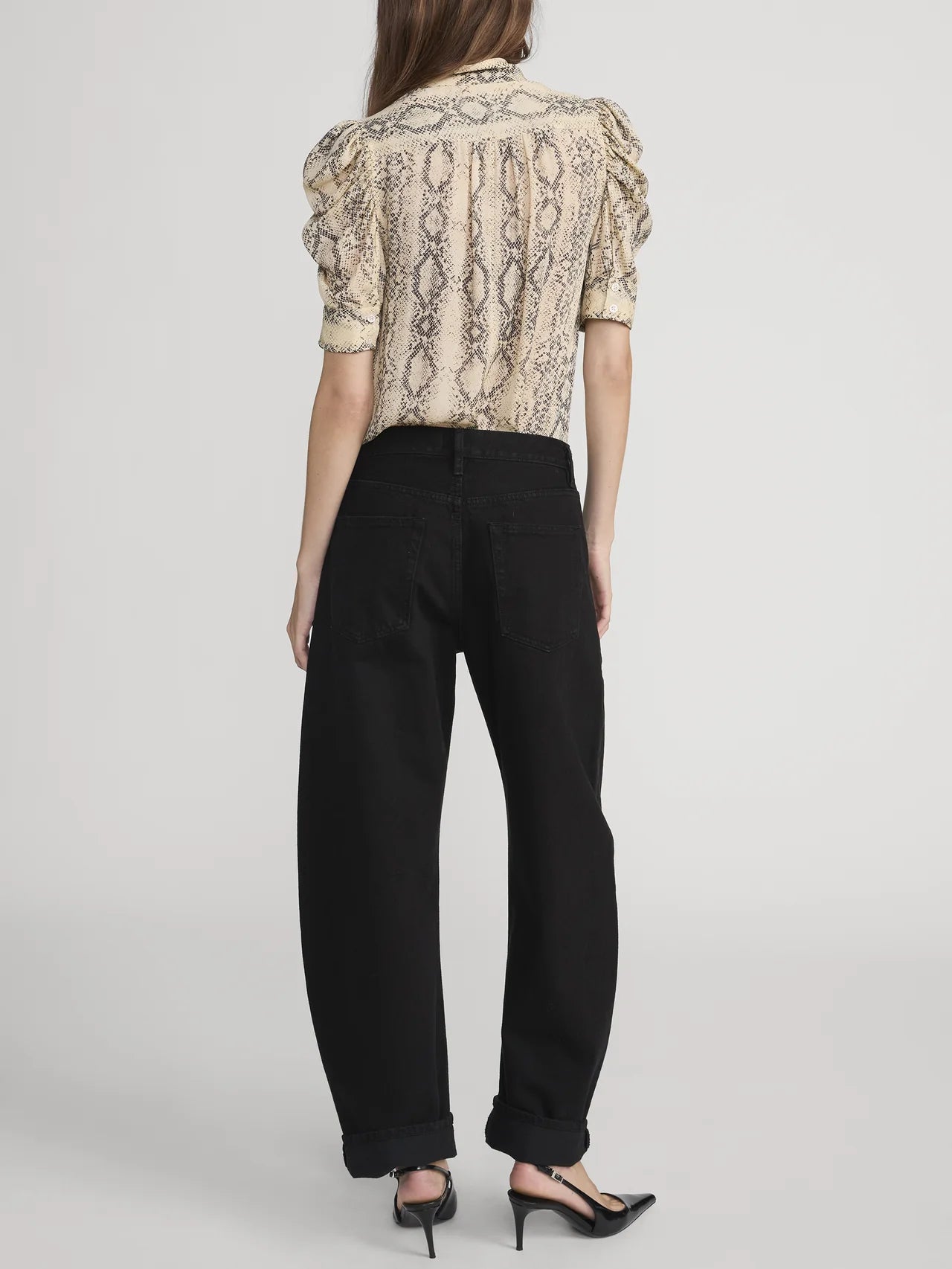 Woman wearing a patterned blouse and black pants on a white background