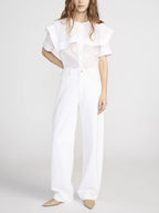 Person wearing a white outfit with a ruffled top on a plain background