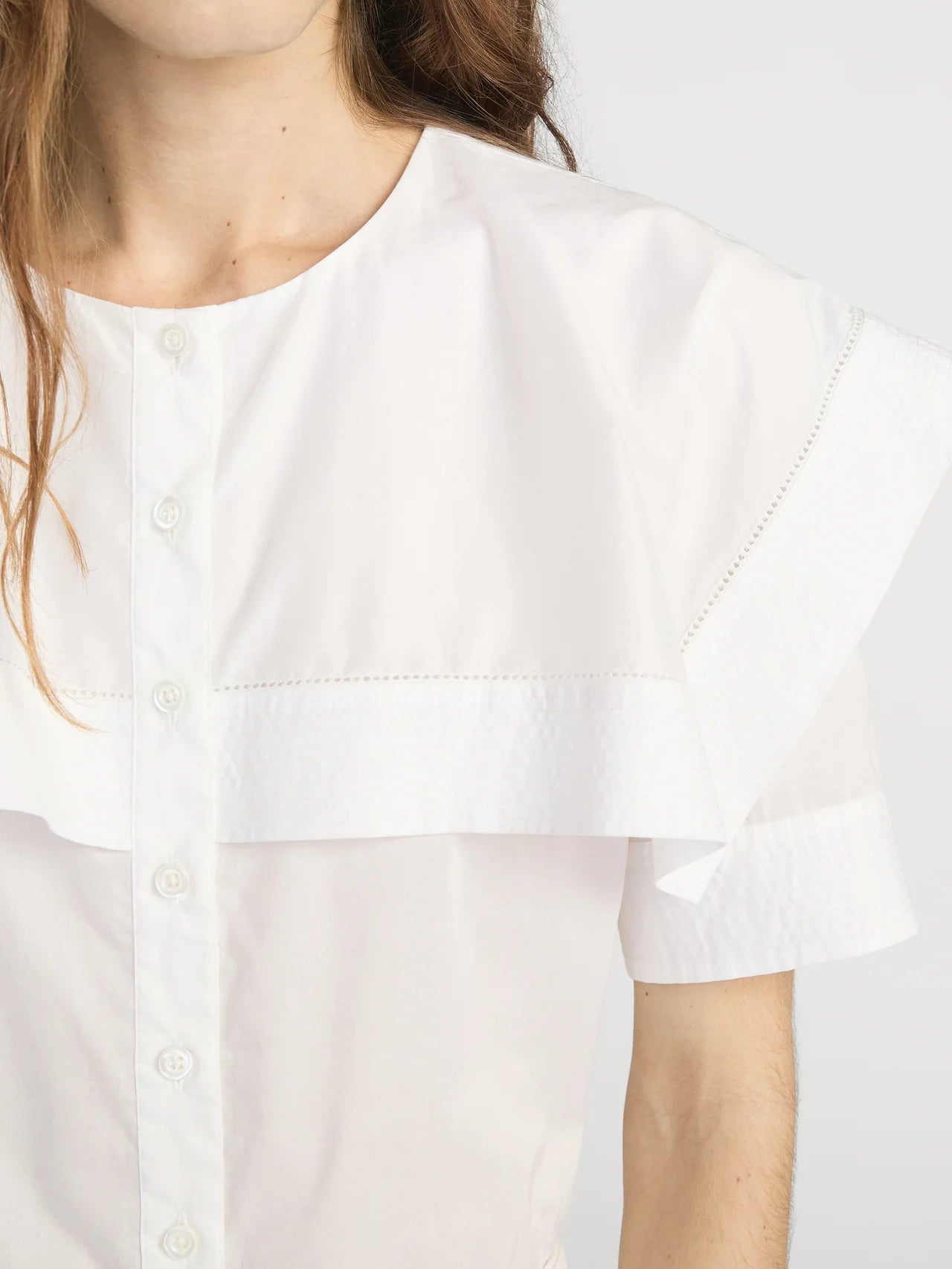 White blouse with short sleeves worn by a person, close-up on the chest and shoulders.