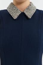 Navy blue dress with a decorative silver collar on a white background