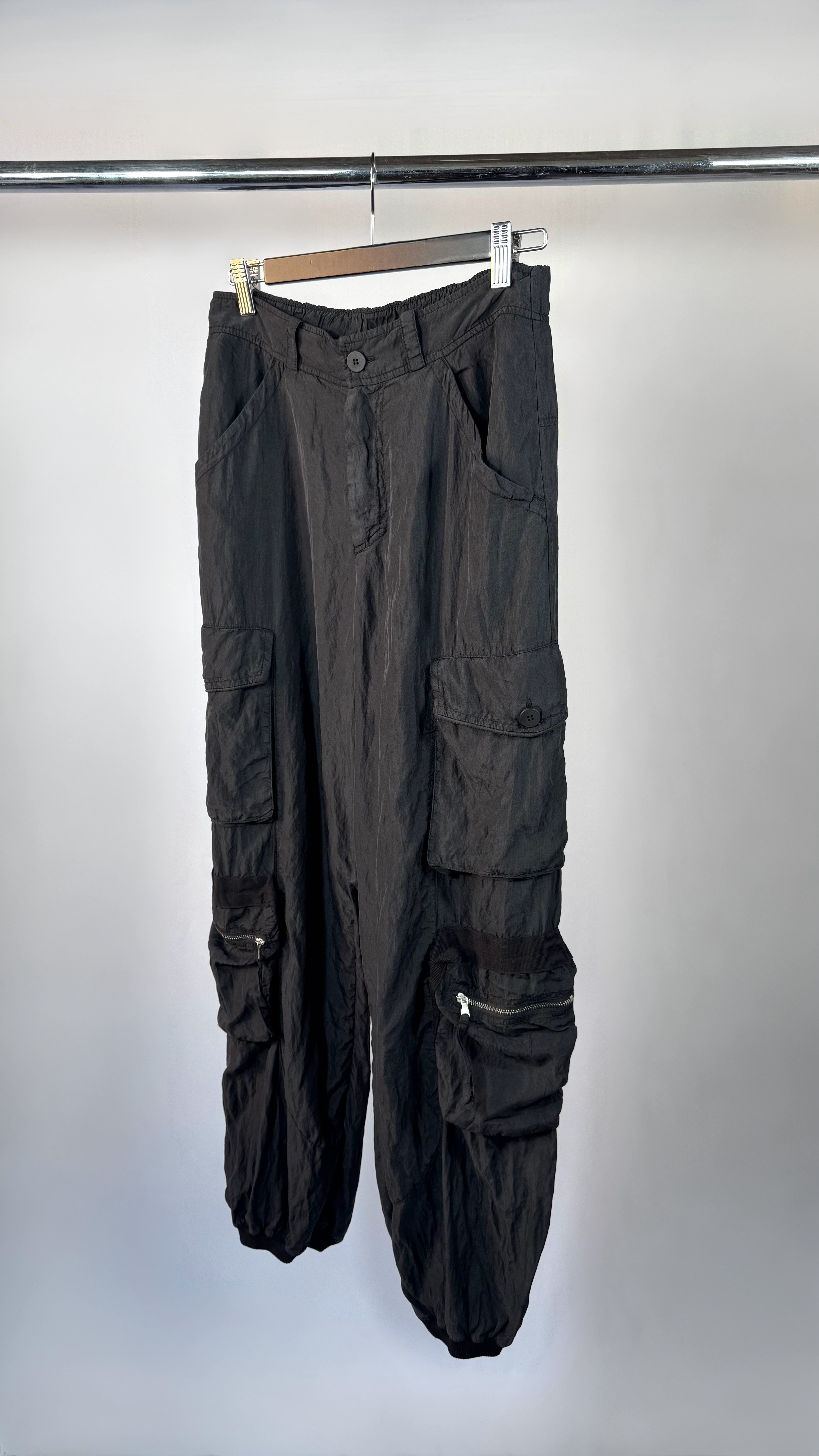 Black cargo pants hanging on a rack against a white background