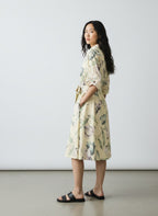 A woman wearing a cream-colored floral print kimono-style dress with a tie waist belt, standing in profile against a plain light gray studio background.
be28st-k.4057
Hannes Roether