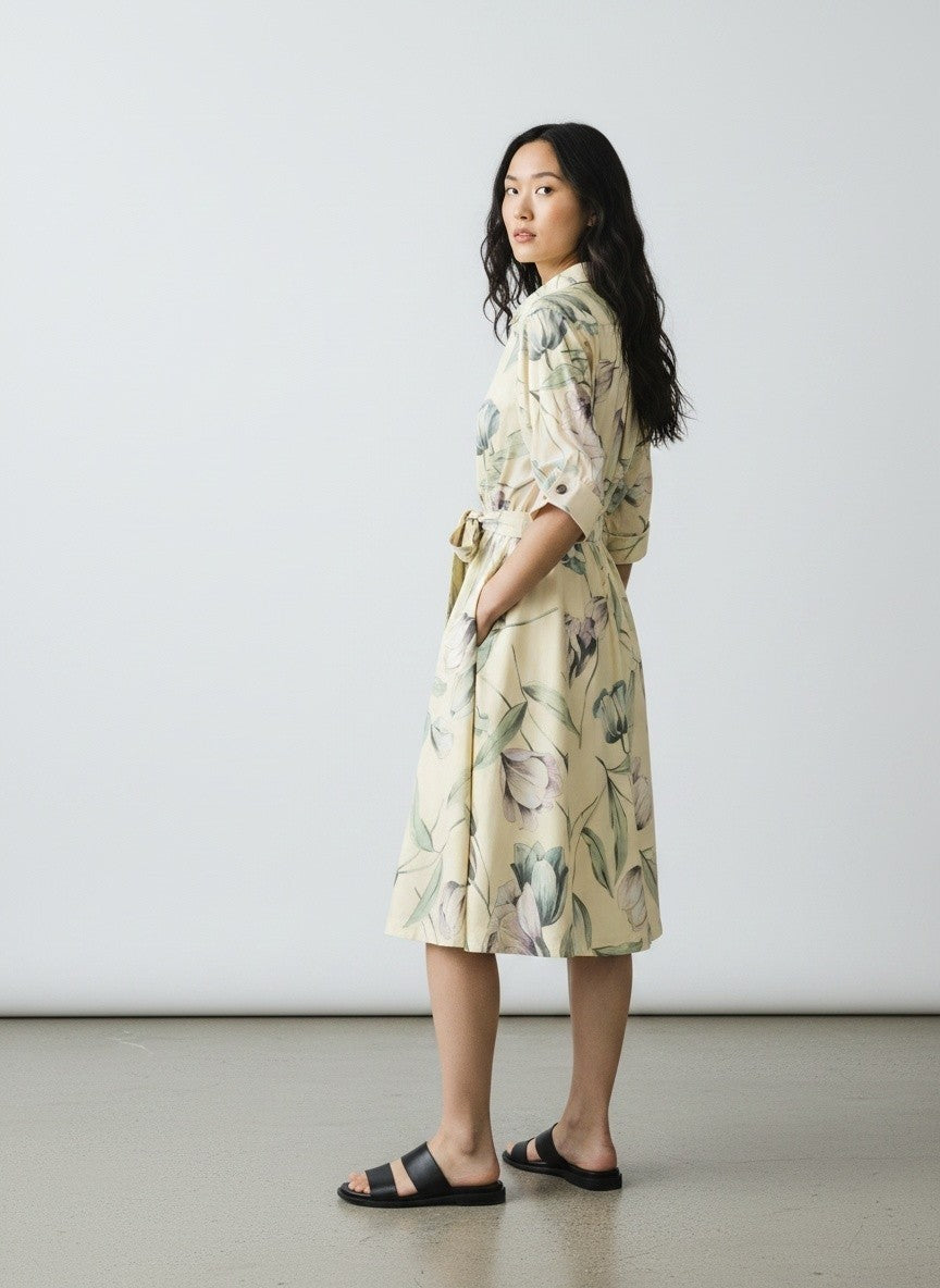 A woman wearing a cream-colored floral print kimono-style dress with a tie waist belt, standing in profile against a plain light gray studio background.
be28st-k.4057
Hannes Roether