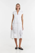 A woman standing wearing a white, V-neck, short-sleeved, long lace dress.