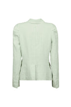 A light sage green linen jacket by Hannes Roether label shown from the back, featuring a high folded collar, long sleeves, and subtle shoulder detailing, displayed against a solid pale blue-gray background.