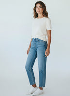Woman wearing a white t-shirt and blue jeans against a plain background