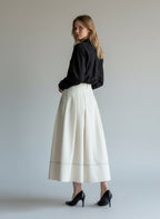 Woman wearing a black top and white skirt against a plain background