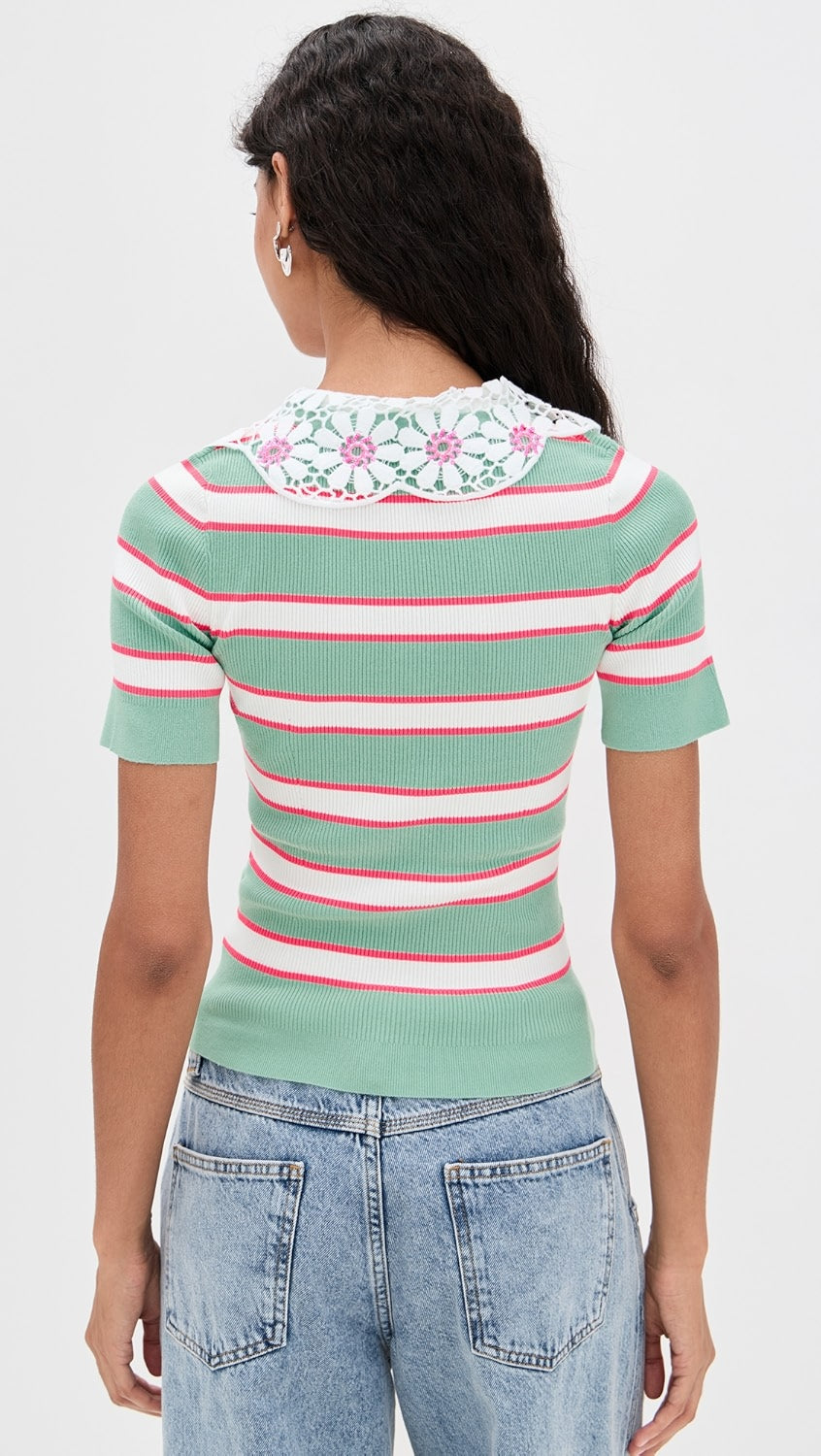 Person wearing a green and pink striped sweater with floral details on a white background