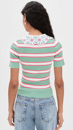 Person wearing a green and pink striped sweater with floral details on a white background