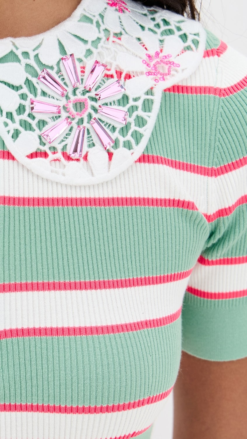 Close-up of a green and pink striped sweater with a floral pattern on the neckline.