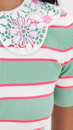 Close-up of a green and pink striped sweater with a floral pattern on the neckline.