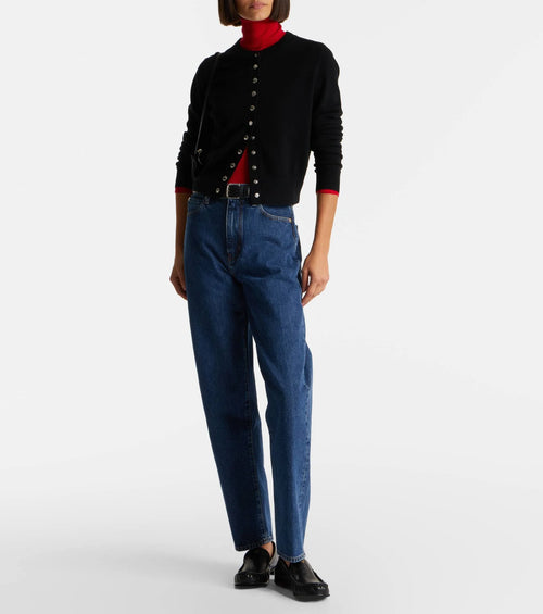 Person wearing a black cardigan, red turtleneck, blue jeans, and black shoes on a white background