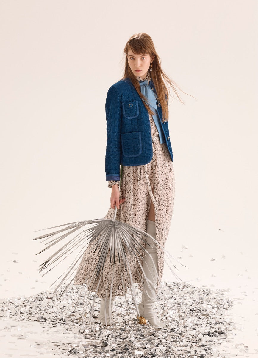 Woman in a blue jacket and beige skirt holding a dried plant on a white background