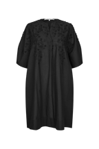 A black short-sleeved tunic dress with intricate floral embroidery and applique detailing on the chest and shoulders, displayed against a solid white background.