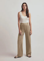 Woman wearing a white tank top and beige pants on a plain background