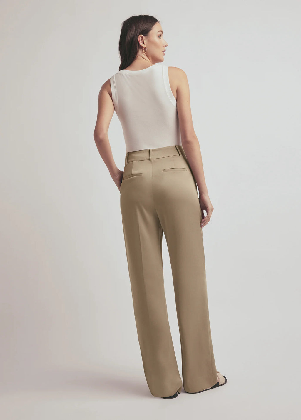 Woman wearing a white sleeveless top and beige high-waisted pants on a plain background