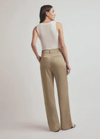 Woman wearing a white sleeveless top and beige high-waisted pants on a plain background