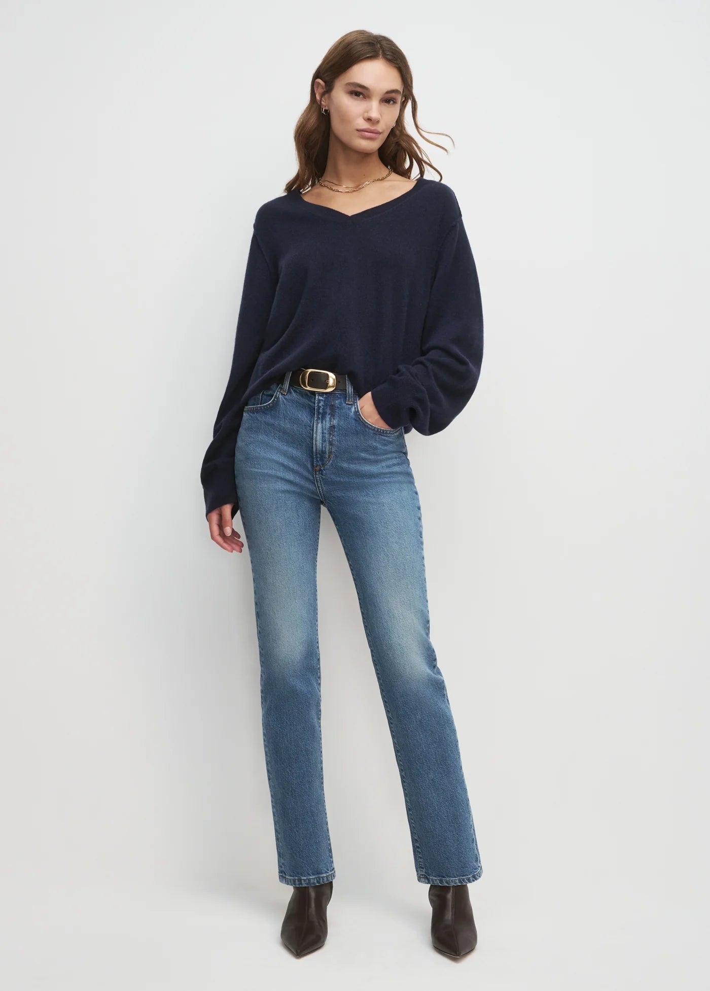 Woman wearing a navy sweater and blue jeans on a white background