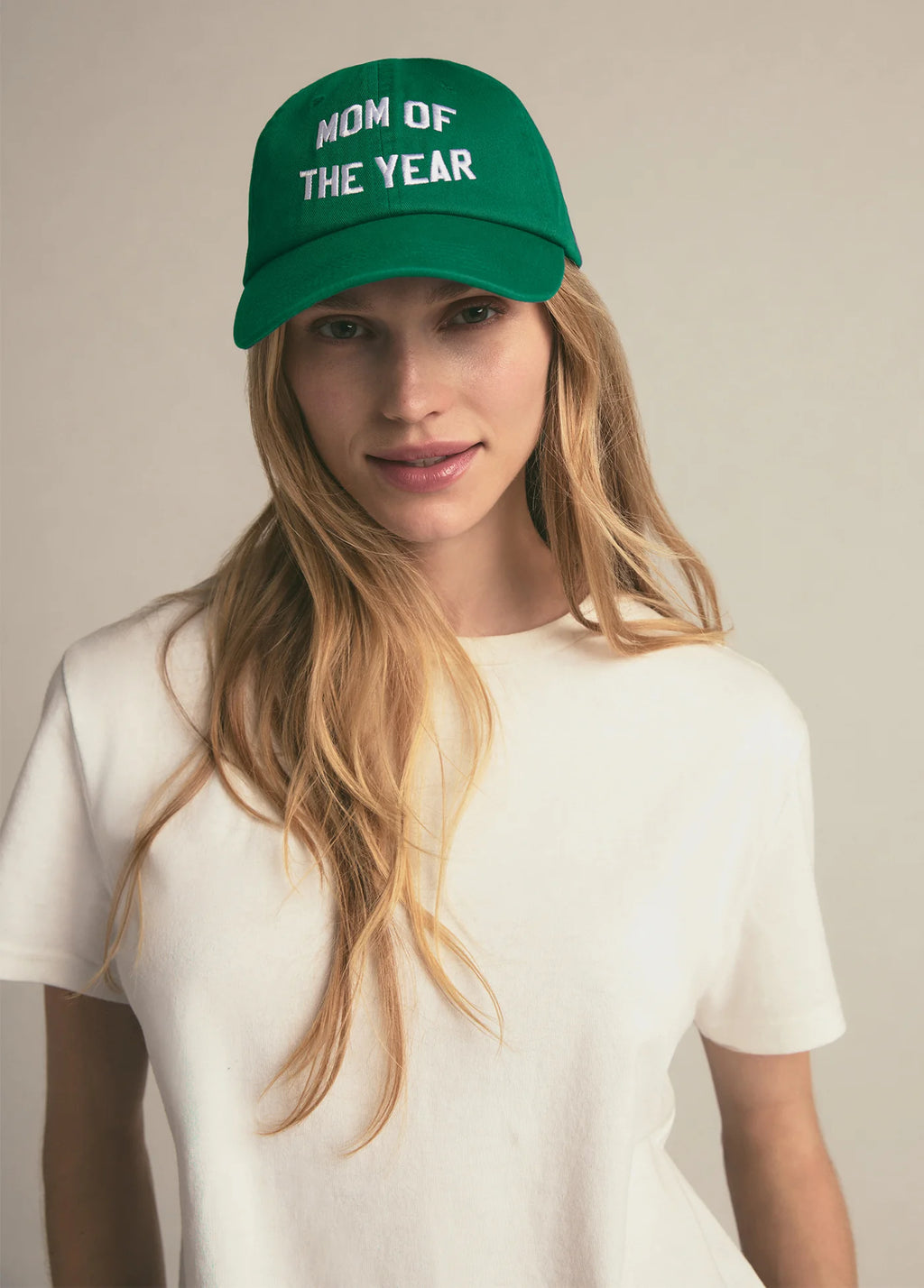 Woman wearing a green cap with 'Mom of the Year' text on a plain background
