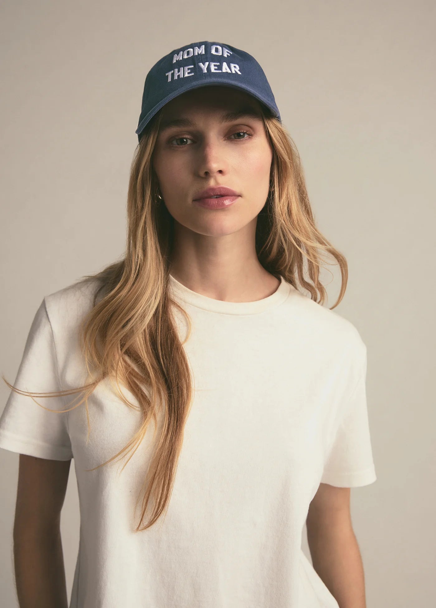 Woman wearing a blue cap with 'Mom of the Year' text on a plain background