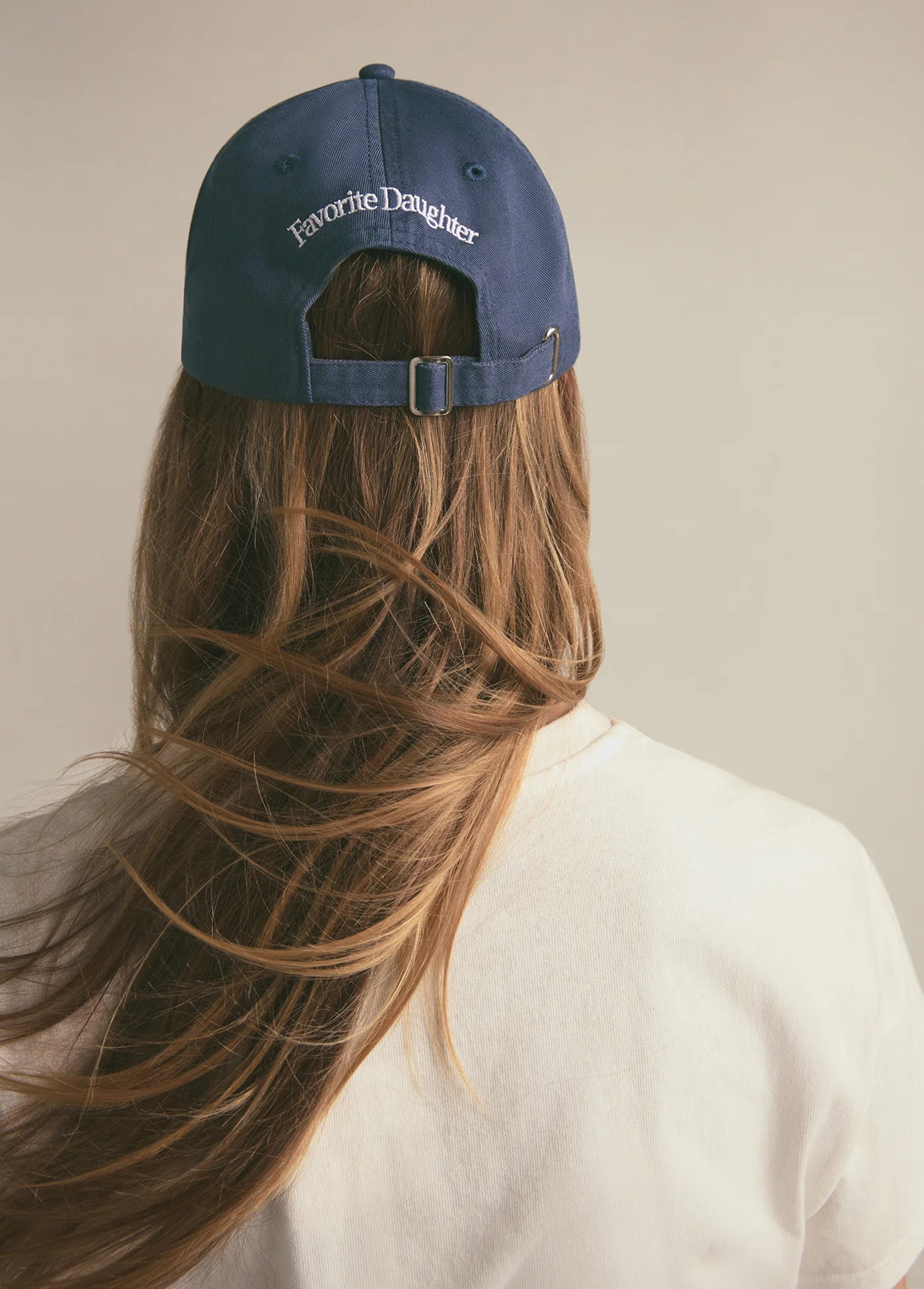 Person wearing a navy blue cap with 'Favorite Daughter' text on a neutral background
