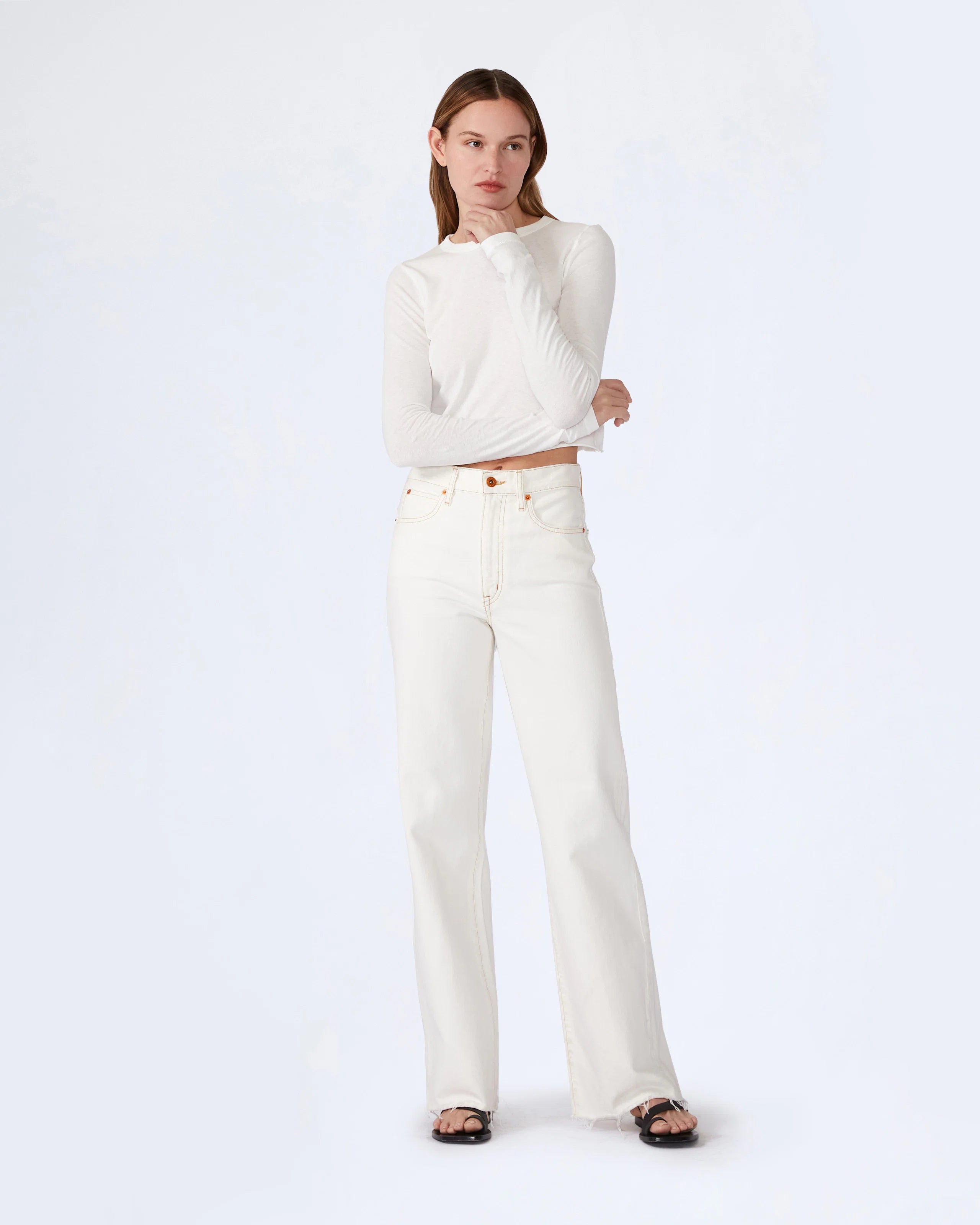 A female model wearing natural white wide leg jeans and a white cropped top.