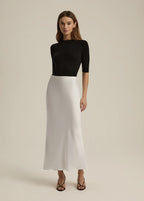 Woman wearing a black top and white skirt on a beige background