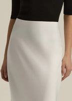 Person wearing a black top and white skirt on a plain background