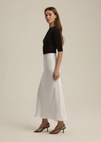 Woman wearing a black top and white skirt on a beige background