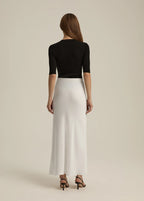 Woman wearing a black top and white skirt on a beige background