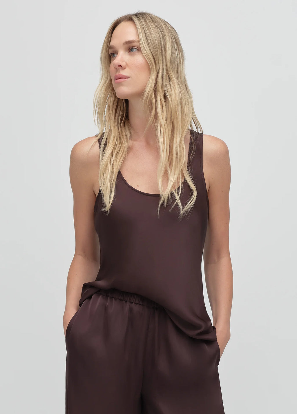 Woman wearing a brown sleeveless top and pants on a light gray background